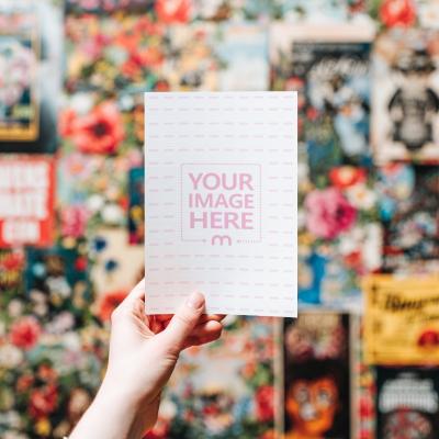 Poster Mockup Held by Hand Against Artistic Poster Wall