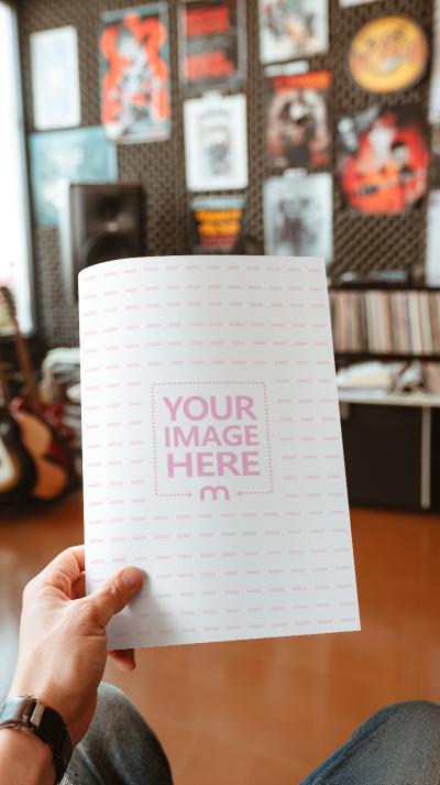 Paper Mockup Held by Hand in Music Studio with Posters in Background