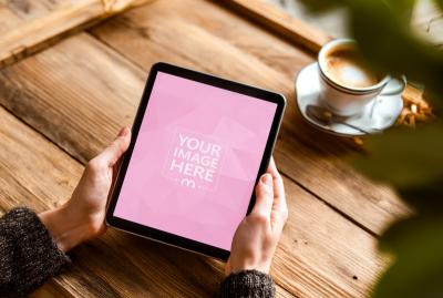 Tablet Mockup Held Over Wooden Table in Cozy Cafe Scene